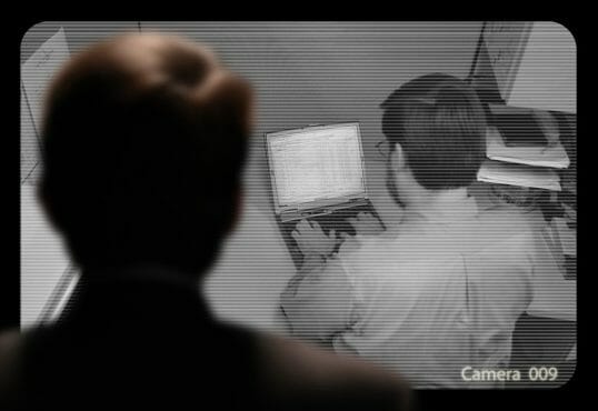 Man observing an employee work via a closed-circuit video monitor Man observing an employee work via a closed-circuit video monitor