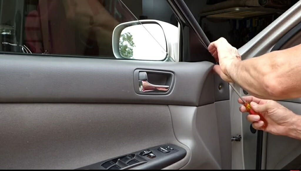 man removing the car's plastic tab using a screwdriver